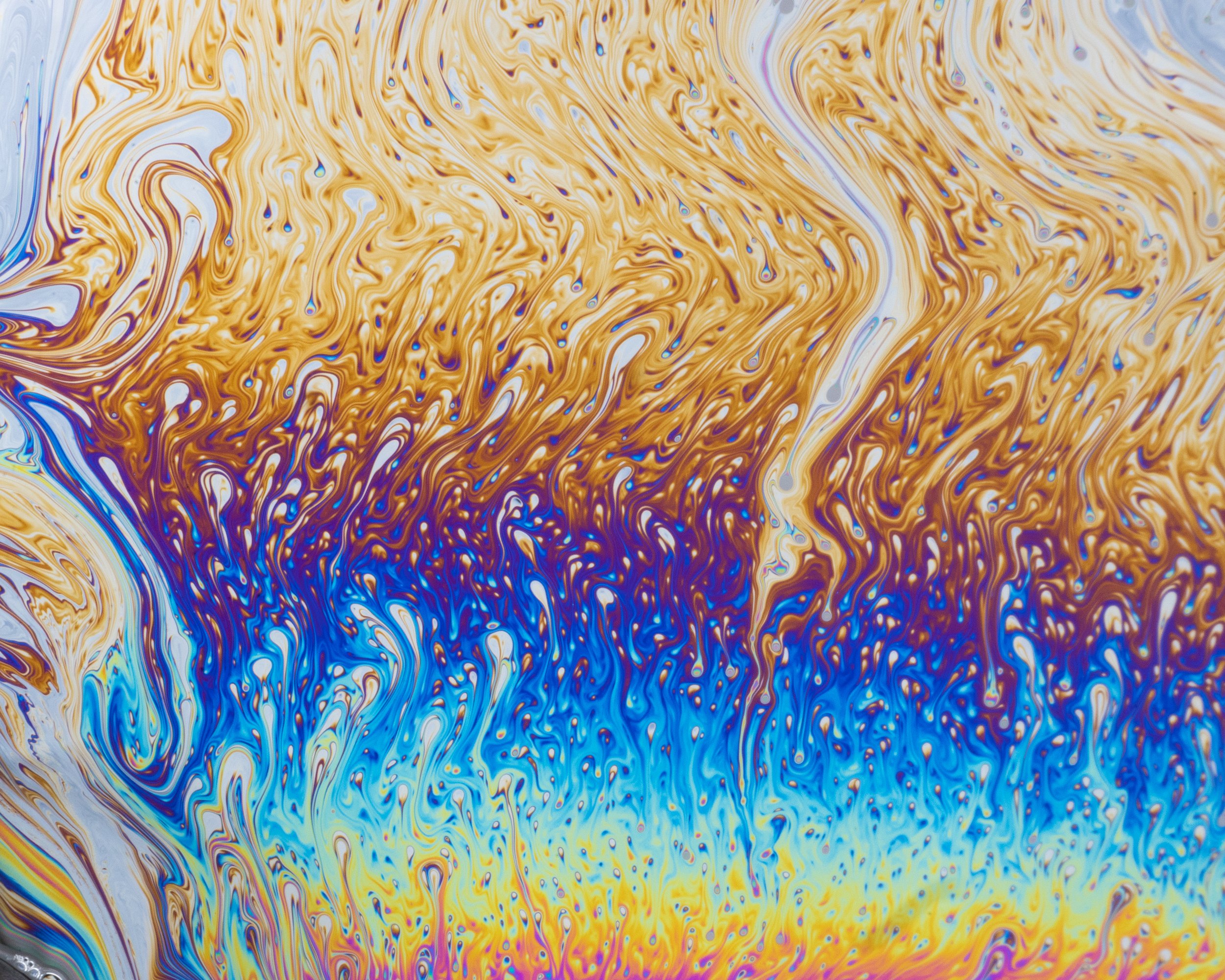 Swirling soap bubble patterns of gold, blue, white, and purple in a marbled abstract design at macro scale.