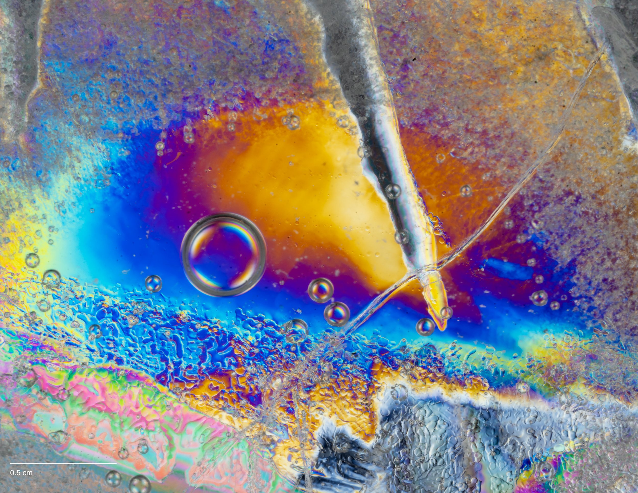 Microscopic image of cross-polarized ice with bubbles and iridescent patterns.