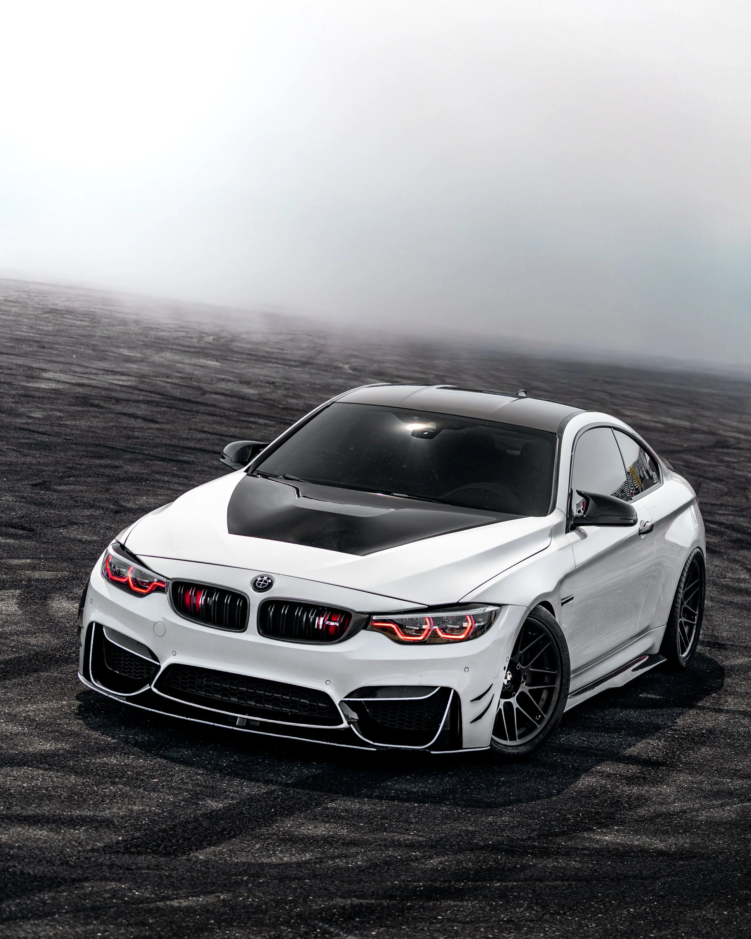 A black and white sports car parked on asphalt pavement with foggy background