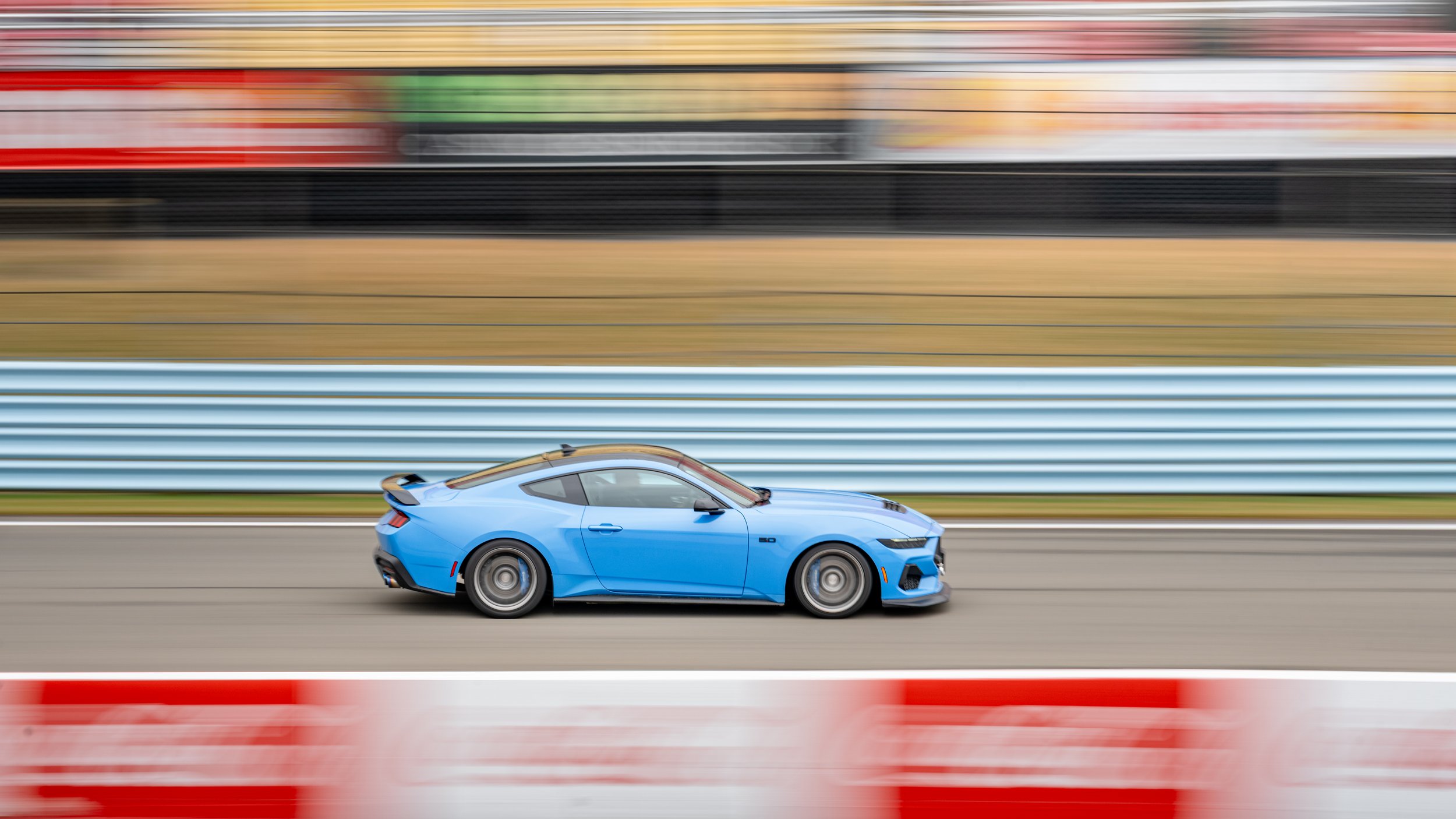 Blue mustang racing on Watkins Glen International with motion blur in the background.