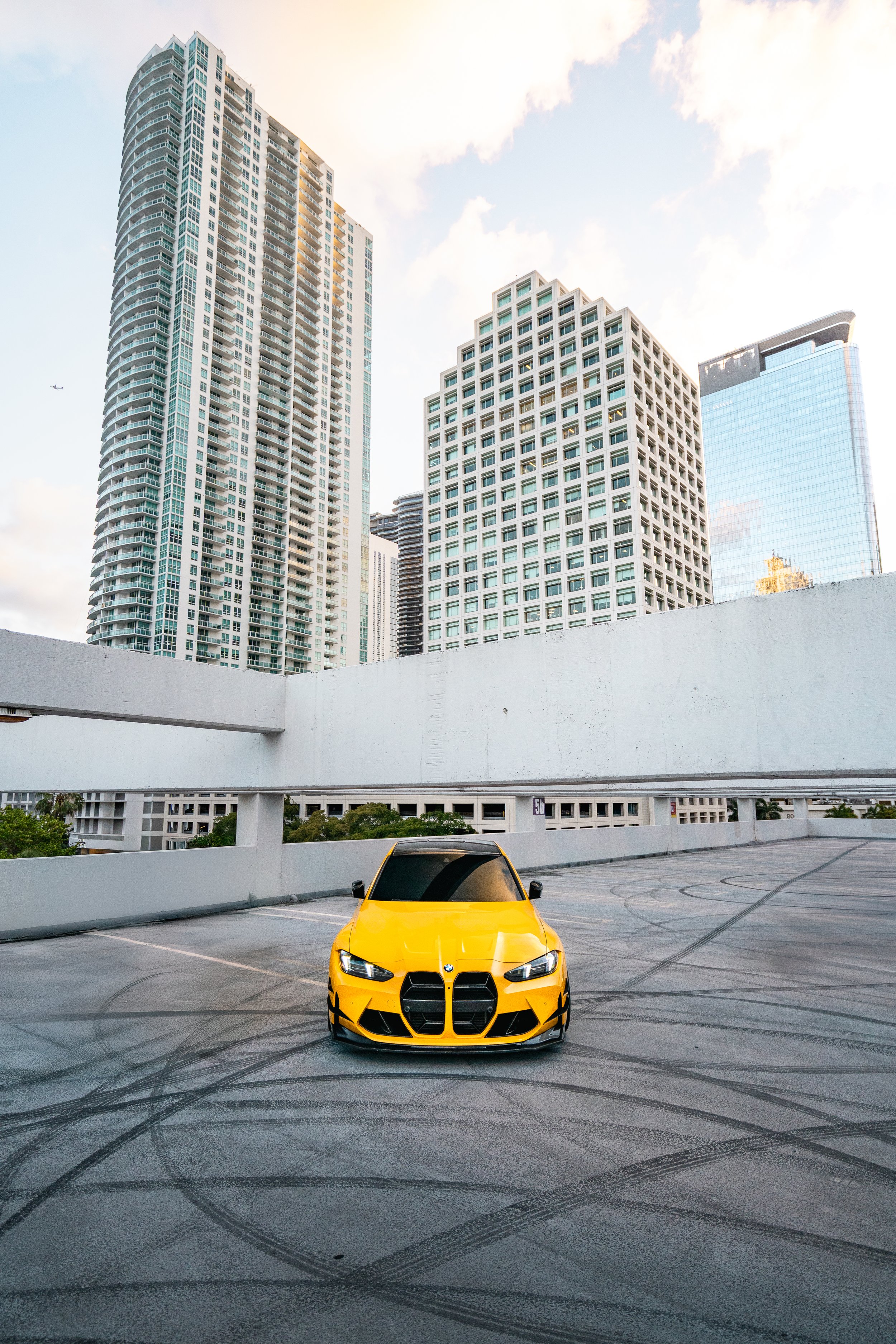 A yellow BMW 2023 G80 custom spec parked in an empty rooftop parking lot with modern skyscrapers in the background during daytime in Brickel, Miami