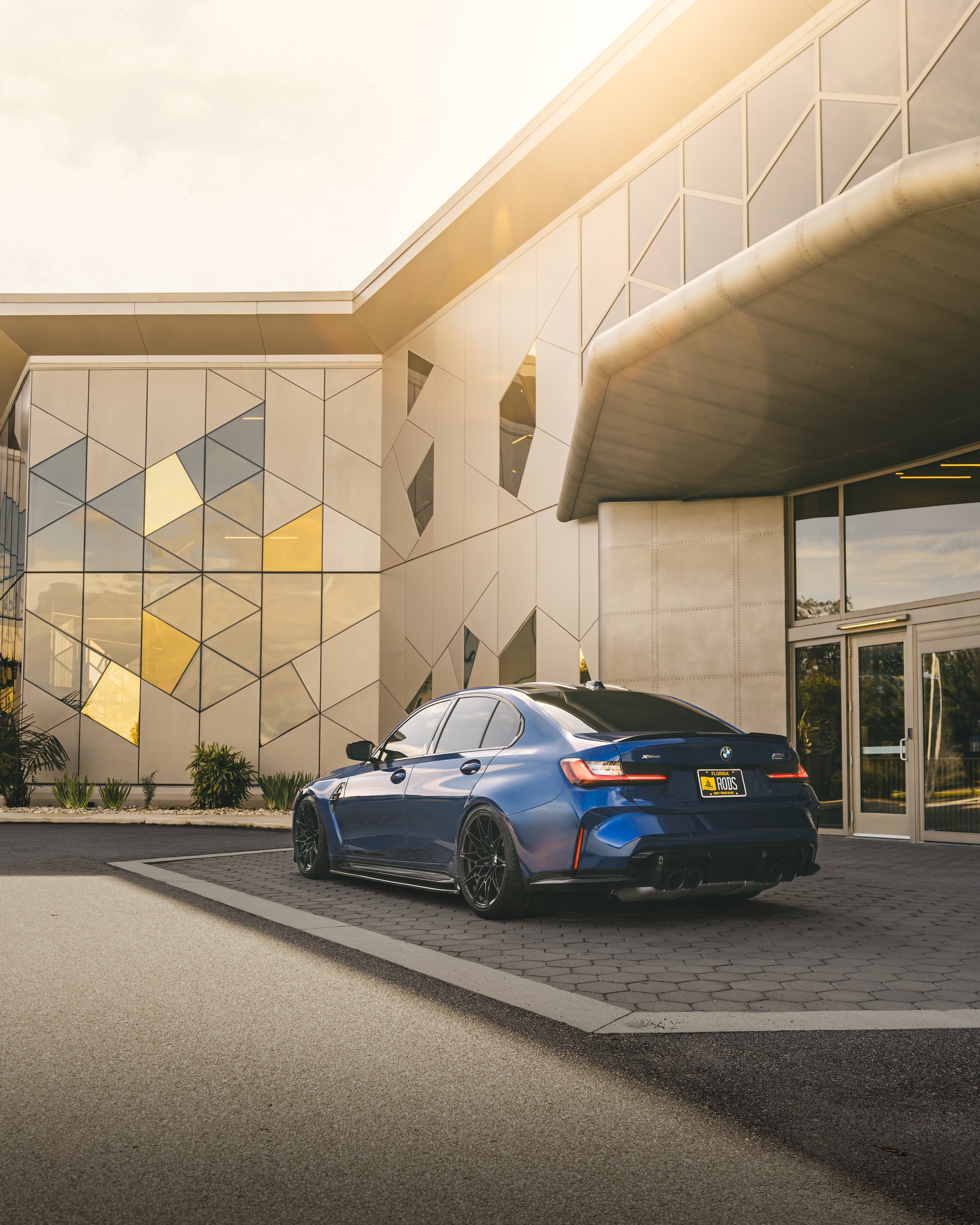 A blue modern sedan parked in front of a contemporary building with geometric glass and metal design