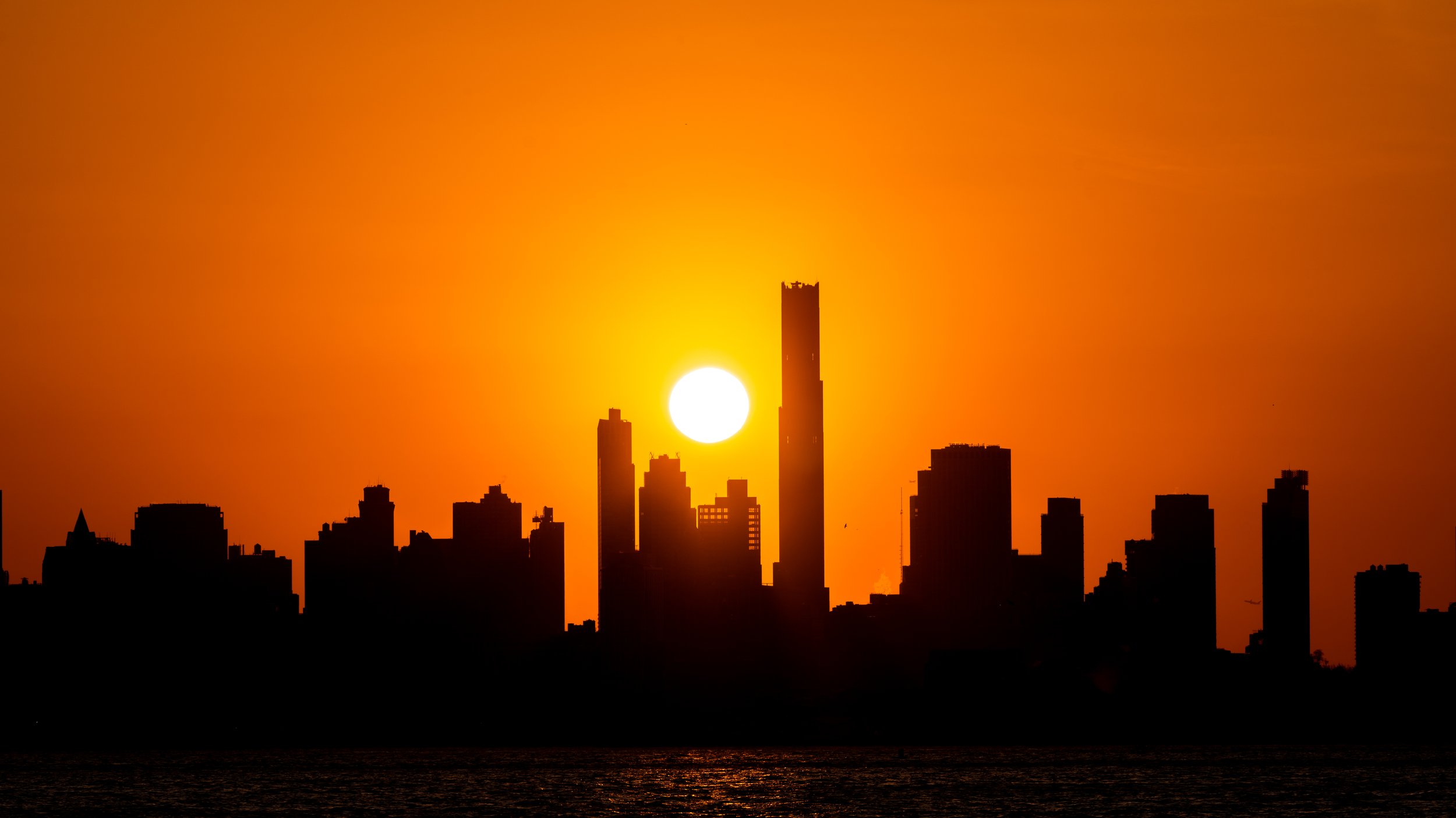 Silhouetted city skyline at sunset with the sun near the horizon and a vibrant orange sky.