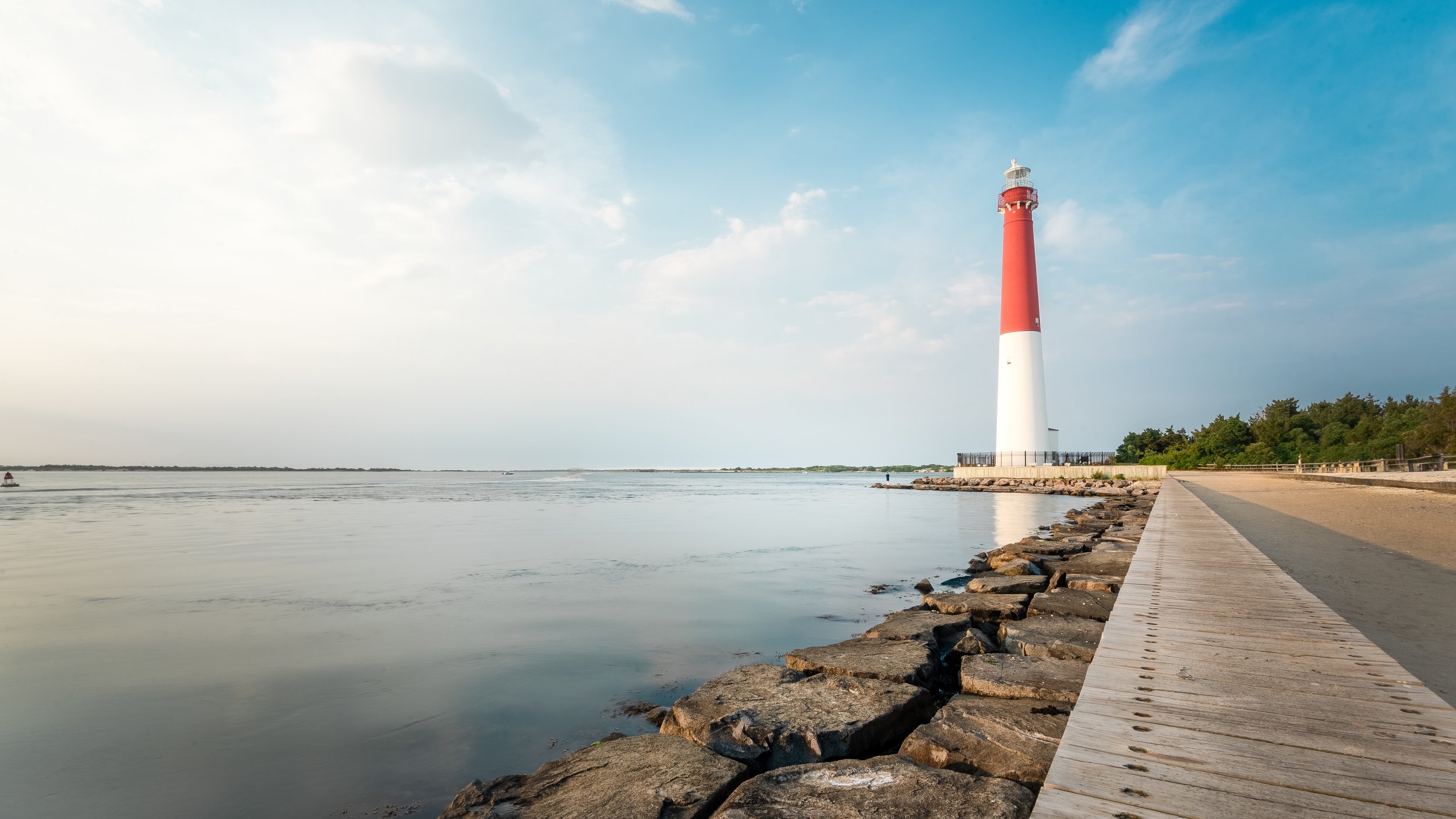 A lighthouse near the water on a clear day with a stone and wooden pathway along the shoreline at Long Beach Island