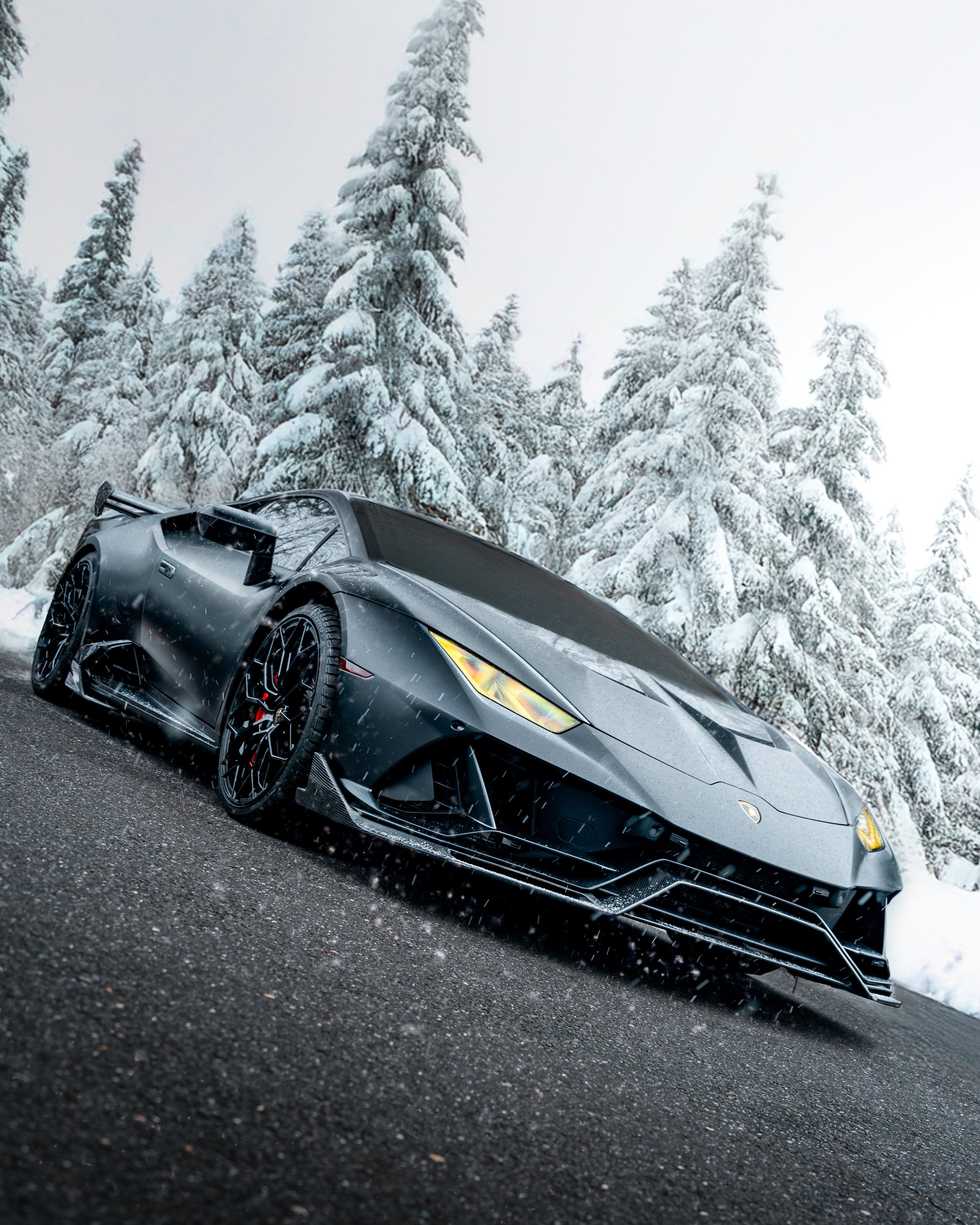 A black Lamborghini Huracan parked on a snow-covered road with snow-covered evergreen trees in the background.