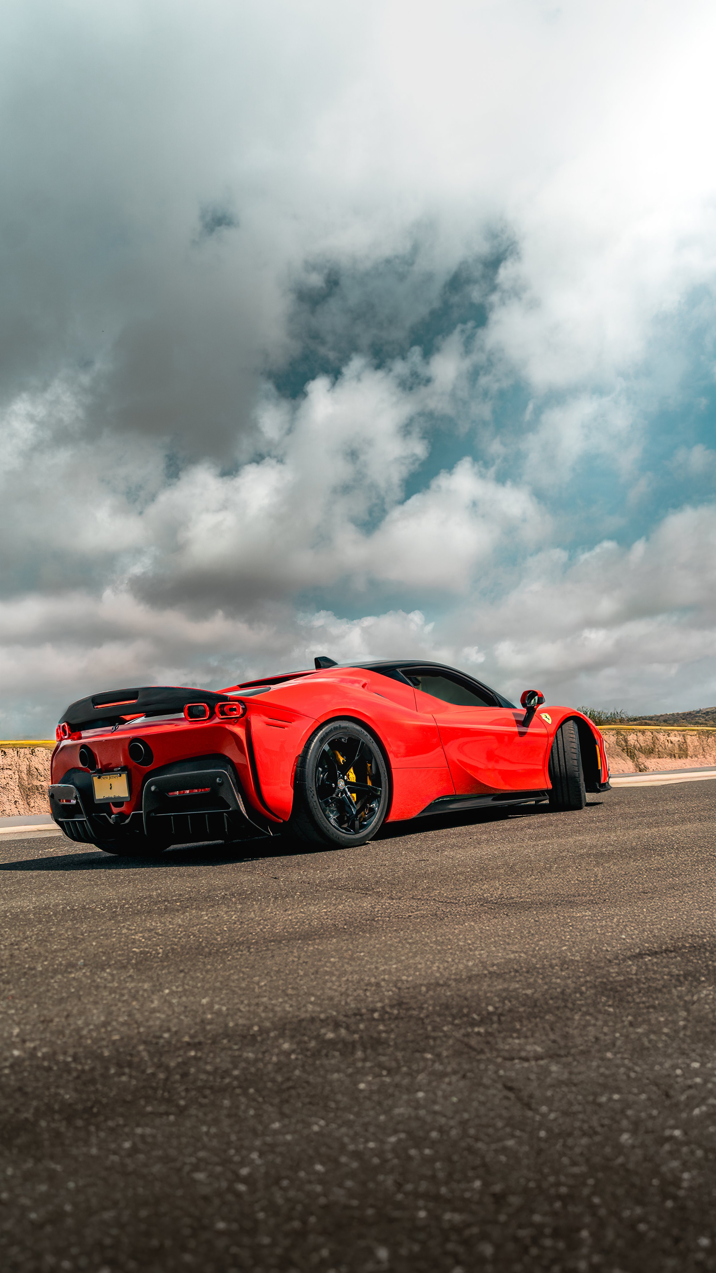 Red Ferrari SF90 parked on a road with a cloudy sky overhead.