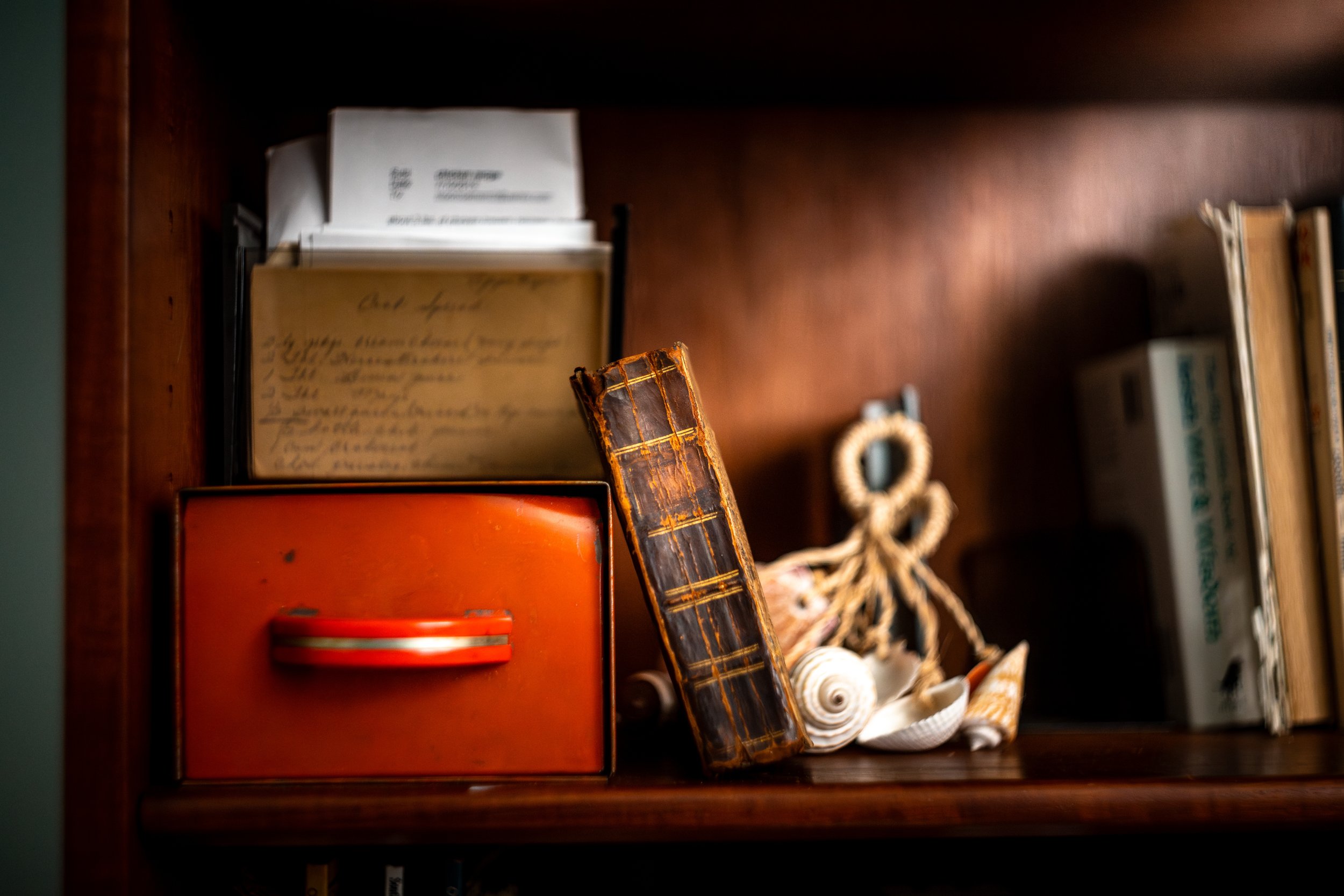 A wooden bookshelf with a red box, a small vintage notebook, seashells, a knotted rope, and books.